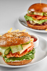 A classic bagel sandwich filled with smoked salmon, cream cheese, lettuce, cheese, and cucumber, served on a white plate against a bright white background with strong shadows.