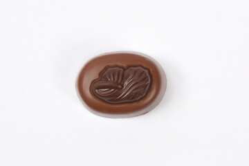 A single, round milk chocolate praline with a cocoa bean embossed design is centered on a plain white background