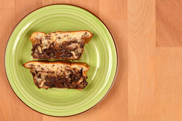 Two thick, rustic slices of moist bread or loaf cake, filled with melted dark chocolate and nuts, rest on a light green plate on a bright wooden surface