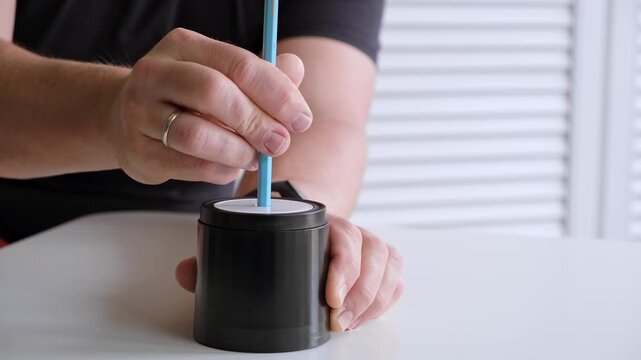 Male hand sticking blue pencil into automatic electric pencil sharpener and sharpening it close-up side view. Office stationery tool. Preparation for drawing and sketching. High quality 4k footage.