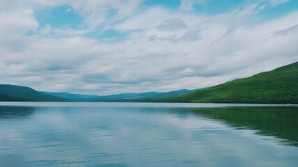 Stunning lake view surrounded by lush green hills under a cloudy sky, perfect for scenic backgrounds, travel promotions, or nature-themed projects