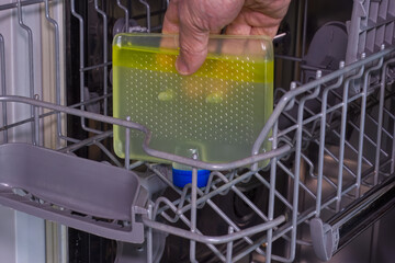 A hand holding container of dishwasher cleaning liquid before closing, used to remove unpleasant...