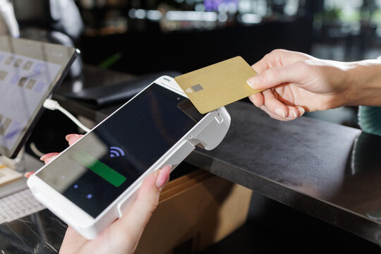 Contactless NFC card tap on POS terminal at bar counter with laptop and tablet