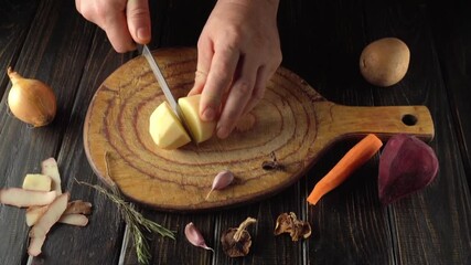 A person is chopping a piece of butter on a wooden board. Surrounding the butter are fresh vegetables such as carrots and beets. The setting is a kitchen with a wooden theme.