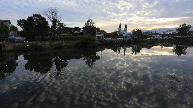 The video background depicts the waterfront, with twilight sky illuminating the riverside community and the lights from houses, reflecting the rural lifestyle of Chanthaburi, Thailand.