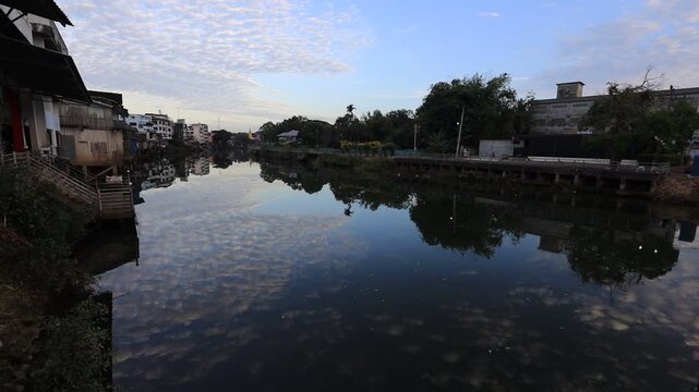 The video background depicts the waterfront, with twilight sky illuminating the riverside community and the lights from houses, reflecting the rural lifestyle of Chanthaburi, Thailand.