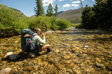 Backpacker Sits On Rock In The Middle of Creek In Remote Grand Teton