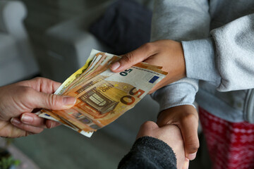 Two women closing a deal, handing over cash and shaking hands; one with light African American skin and the other Caucasian. Corruption