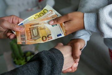 Two women closing a deal, handing over cash and shaking hands; one with light African American skin and the other Caucasian. Corruption