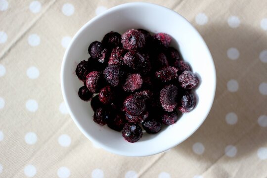 Close-up overhead view of a bowl of frozen blueberries on a polka dot tablecloth