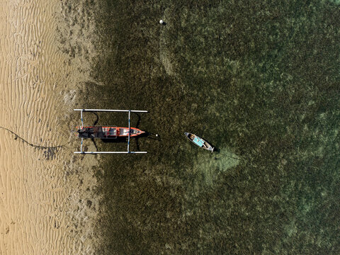 Aerial view of a Traditional Balinese Outrigger Boat (juking) and rowing boat in the sea at low tide, Bali, Indonesia