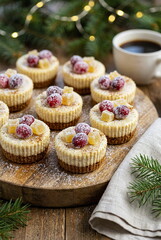 Gingerbread spiced mini cheesecakes, creamy texture with gingerbread crust. Small Christmas decorations like cranberries or candied ginger, served on a rustic wooden board,