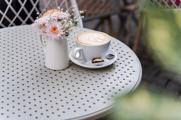 Close-up of a cappuccino and date stuffed with spicy orange butter on a garden table next to a bunch of flowers
