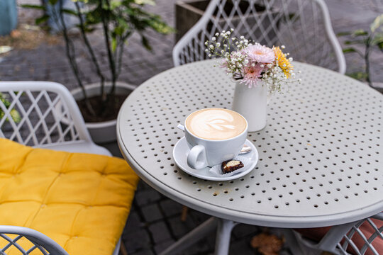 Close-up of a cappuccino and date stuffed with spicy orange butter on a garden table next to a bunch of flowers