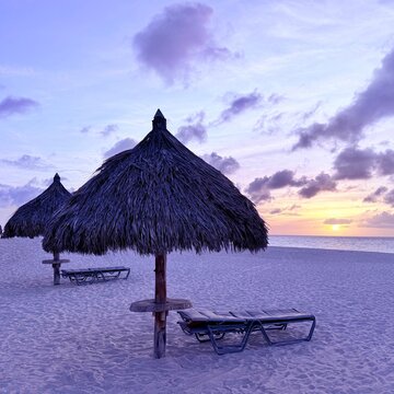 Two sun loungers and straw parasols on a sandy beach at sunset, Eagle Beach, Aruba