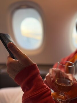 Close-up side view of a man on an aircraft using his mobile phone and drinking a glass of wine