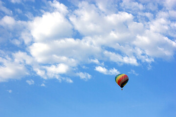 Multi coloured hot air balloon in flight in a blue sky with clouds