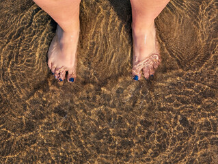 Personal perspective overhead view of a Woman standing barefoot in the Mediterranean Sea, Italy