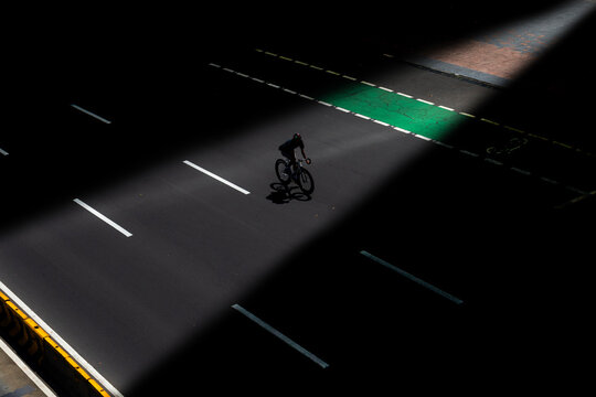 Ray of light illuminating a cyclist riding his bike along an empty city road, Indonesia
