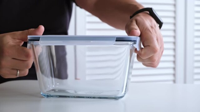 A man is opening the glass food container with a plastic lid with snaps. The concept of convenient bowl for safe. Reusable tableware for storage, baking and freeze. High quality 4K footage.