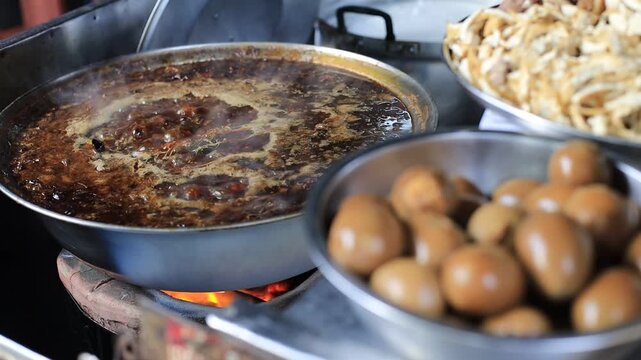 The video background shows Tawan cooking over a charcoal stove, the aroma enticing and delicious, the kind of noodle soup or kway chap commonly sold in tourist areas.