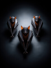 Three black bats with orange ears hanging in dark background creating spooky Halloween mood