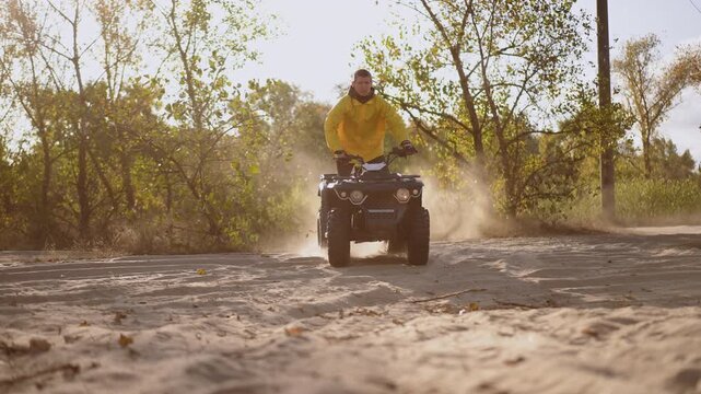 ATV rear spinning through sand and dust plume, trail guide in yellow jacket carves tight turn beneath trees, closeup tire churn sends cloud of particles