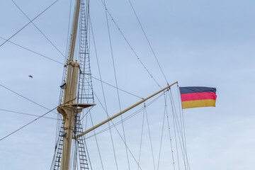 Seagull flying in sky near ship mast with German national flag