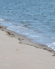Waves gently lap at the sandy shore of a tranquil beach in bright sunlight during early afternoon