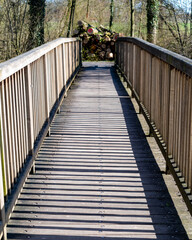 Fototapeta premium Wooden bridge leading through trees with logs stacked at the end during a sunny day