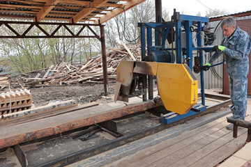 Wood processing at a sawmill. A professional carpenter uses a machine for sawing wooden planks. Lumber is in stock. Production concept.