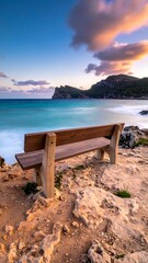 Coastal bench faces turquoise sea under a colorful sunset sky, serene and inviting for peaceful contemplation