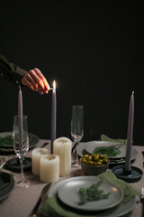Lighting candles on an elegant Christmas dinner table with olives and rosemary