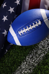 Football on a green field with white stripe and American flag behind