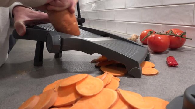 Stockholm, Sweden A home chef slices sweet potatoes on a Mandolin in a residential kitchen. 