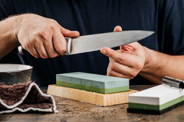 A man sharpens a knife with a grindstone on a rustic wooden table.