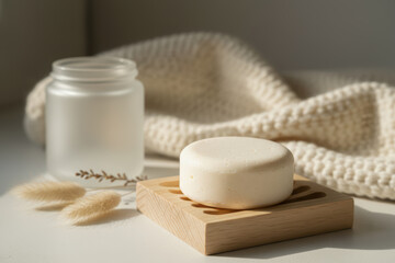 Zero waste solid shampoo bar on a wooden dish with frosted jar, dried flowers, and a knitted blanket in natural light