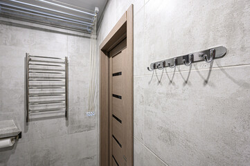 Bathroom with gray tile walls, wooden door, chrome towel rack, and radiator, featuring a minimalist and contemporary design aesthetic