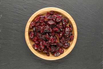 Dried cranberries in a wooden saucer on a slate stone, top view, macro.