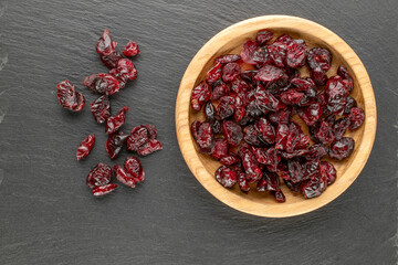 Dried cranberries in a wooden saucer on a slate stone, top view, macro.