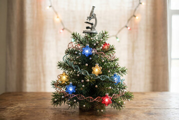 Miniature christmas tree decorated with colorful dna helix garland, glowing science themed lights, and microscope tree topper