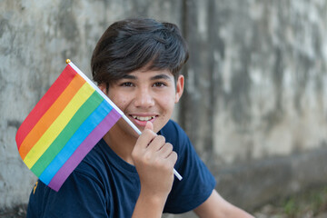 Teenaged boy wears rainbow wristband and holding rainbow flags, lgbtqai symbol, in front of wall, concept for calling out all people to respect human rights of lgbtqai people around the world.