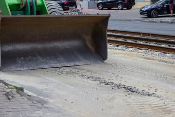 A bulldozer bucket on the road. Rails and asphalt road. Roadworks.