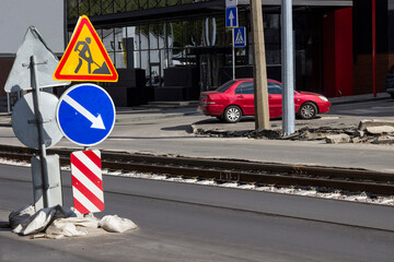 Roadside safety signs during road repairs. Tram track, red car behind lampposts.