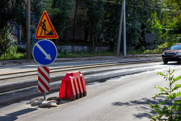 Road signs during road repairs. Tram tracks and a car on the road.
