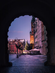 Winter City Square Framed by Archway With Christmas Tree, Historic Clock Tower and Cozy Caf&eacute; Lights at Dusk In Old Town, Gdansk, Poland