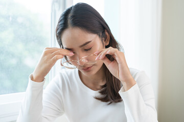 Eye problem concept, fatigue asian young woman tired eyes, irritated rubbing eye dry relief vision pain after work on laptop computer, eye strain, hand holding glasses, suffer migraine, bad blurry.