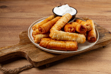 fried spring rolls with cheese, on a wooden background, with cream sauce, no people,