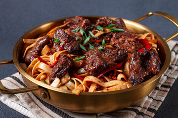 Udon noodles with beef in Mongolian style, with green onions and vegetables, homemade, on a dark background,