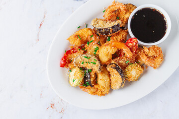 Shrimp and vegetable tempura, served with dipping sauce, on a white plate